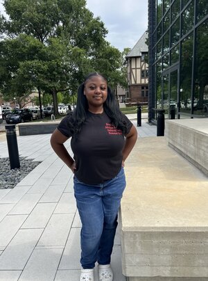 a black woman in jeans and a black t - shirt standing in front of a building.