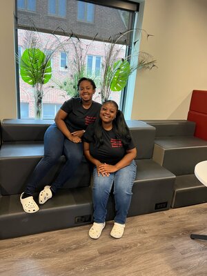 two Black women sitting on a bench in an office.